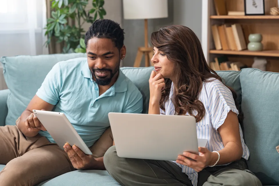Two people reviewing information together on a laptop and tablet at home.