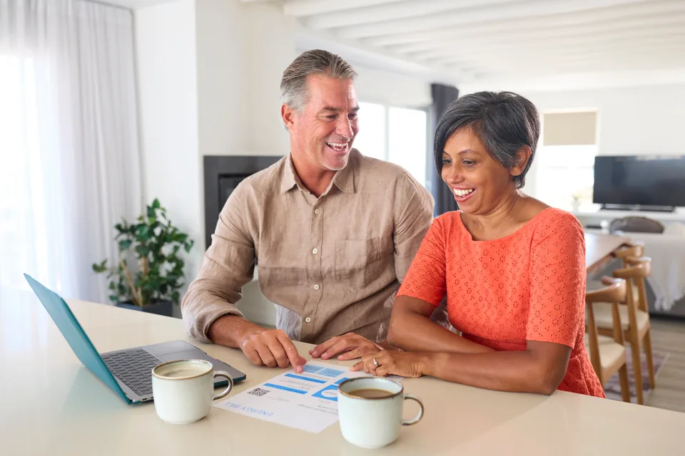 A couple at home looking at an energy bill beside their laptop.